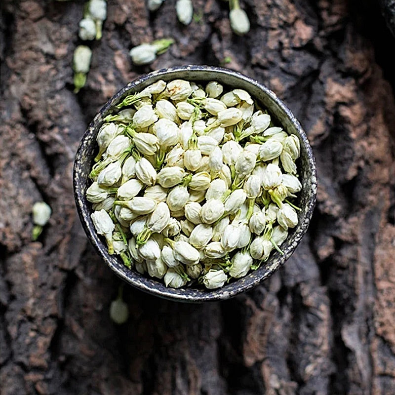 Bulk dried jasmine tea blossoms in a bowl on rustic wooden background.